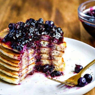 Stack of Lemon Poppy Seed Pancakes with Blueberry Compote on a white plate with fork
