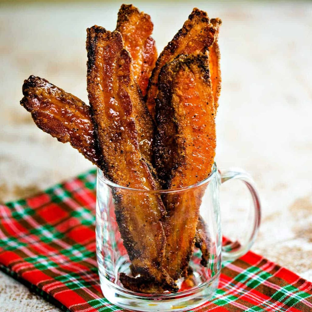 pieces of candied bacon in a glass mug on a red and green plaid napkin