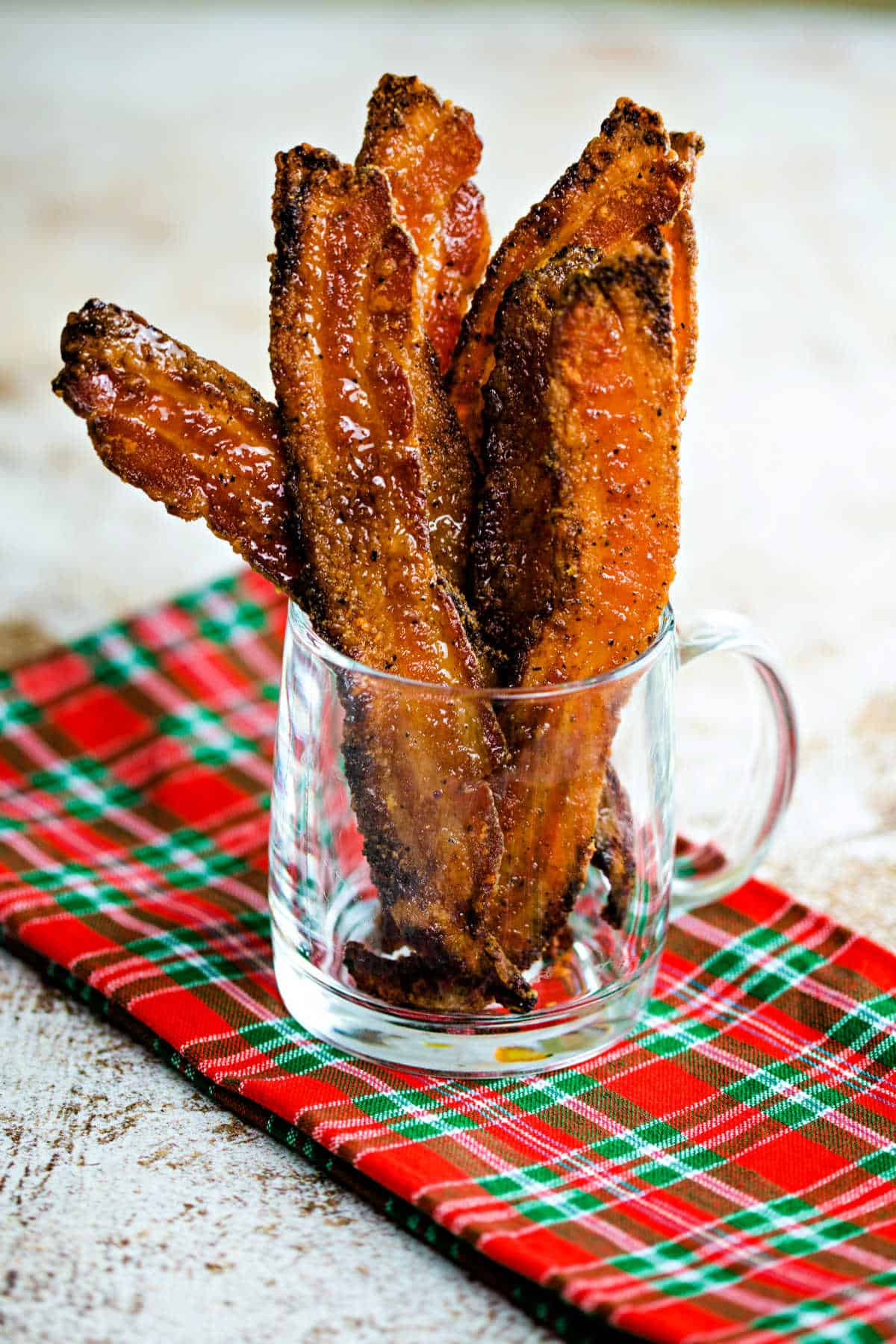 slices of candied bacon in a glass mug sitting on a green and red napkin