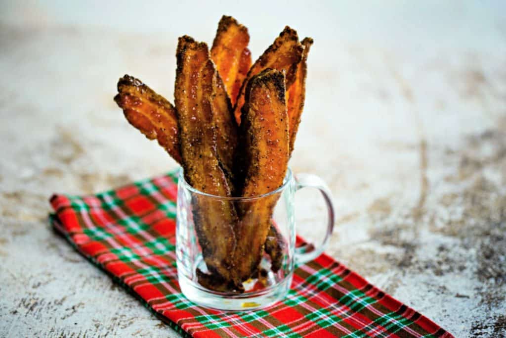 slices of sugared pepper bacon in a clear glass mug