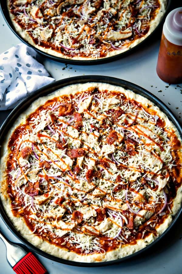 two barbecue chicken pizzas ready for the oven in round pizza pans