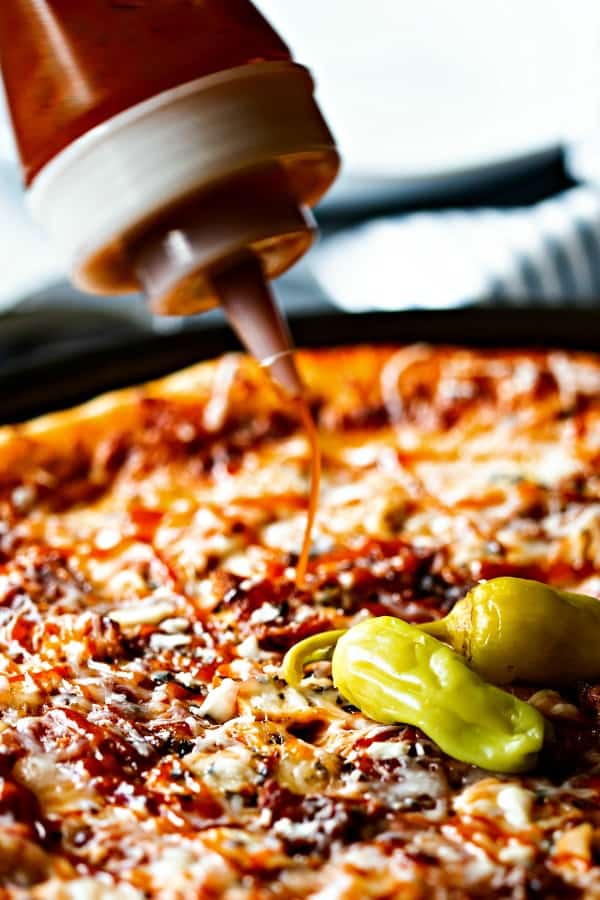 a squirt bottle with barbecue sauce being drizzled on a pizza