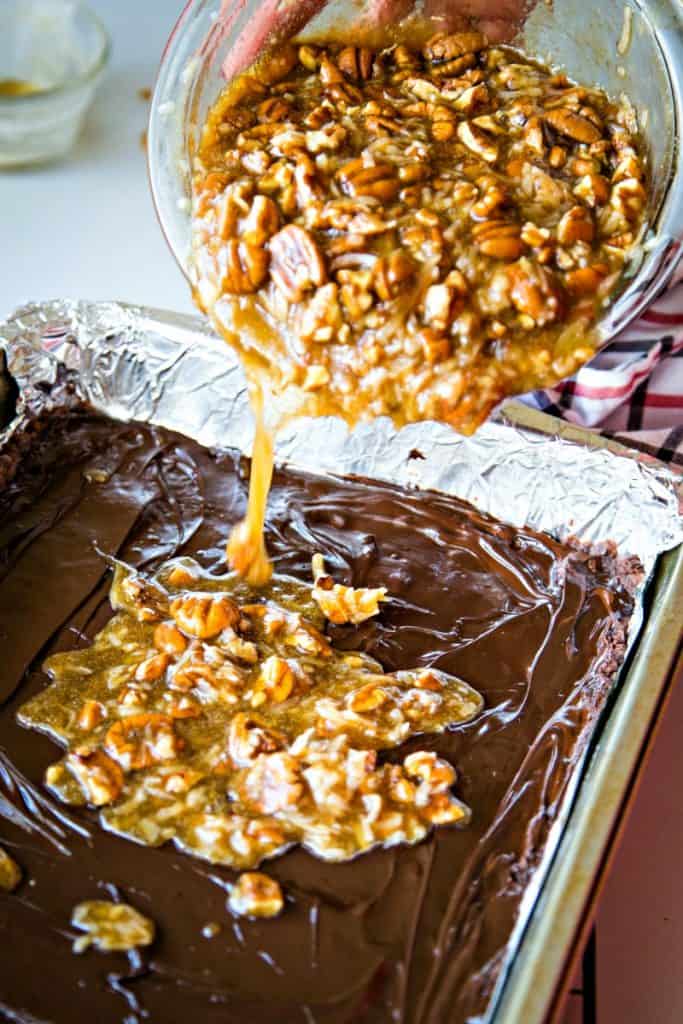 Chocolate batter in a pan being topped with pecan pie filling