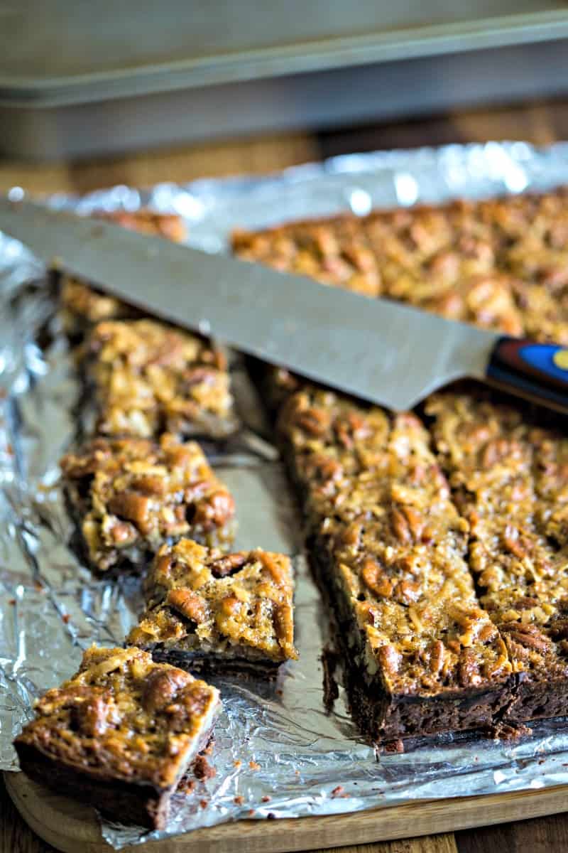 a chef's knife cutting German pecan pie bars on a piece of aluminum foil