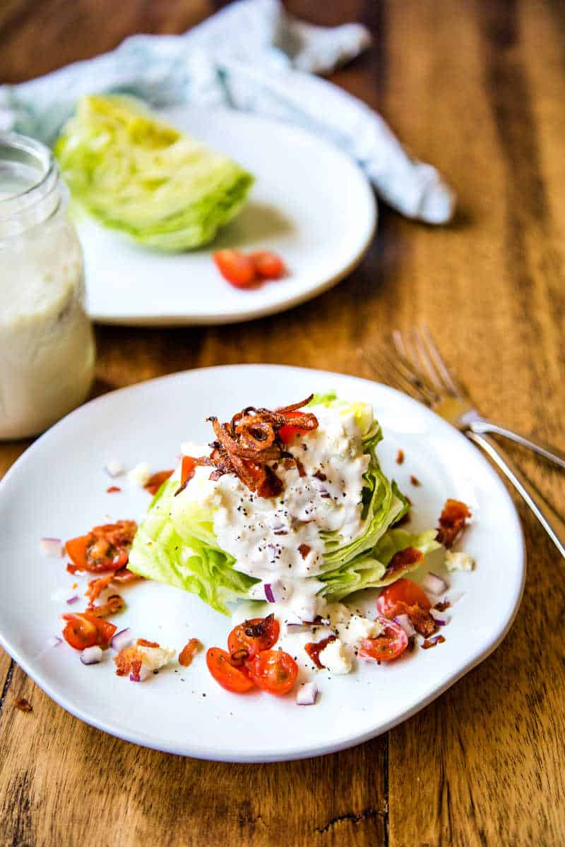 wedge salad on a withe plate with chopped tomatoes, bacon, and crispy shallots