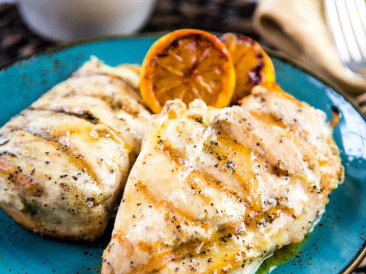 two grilled chicken breasts garnished with charred lemons on a blue plate