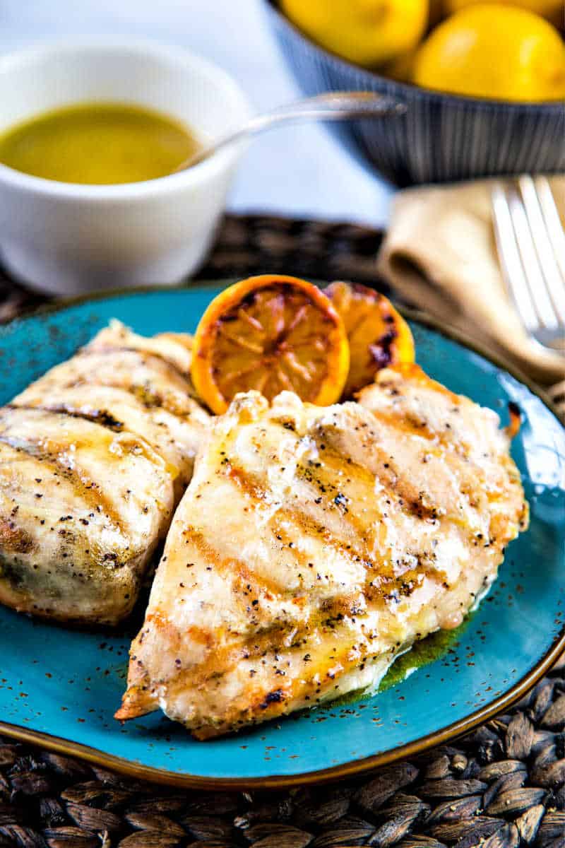 two grilled chicken breasts on a blue plate with lemons