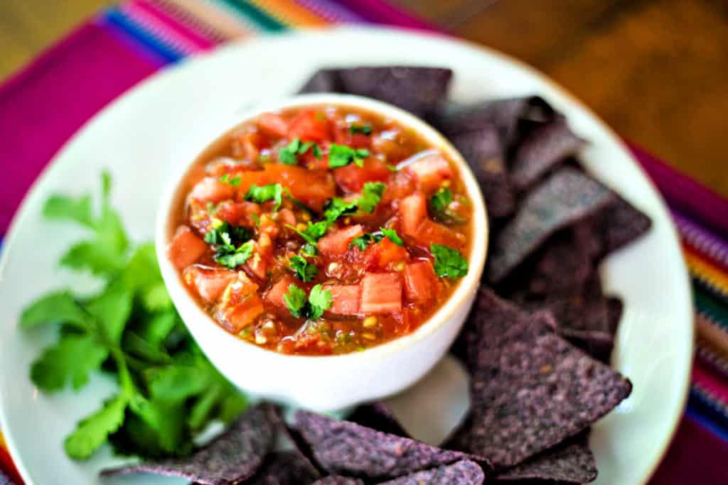 fresh tomato salsa on a white platter with cilantro and blue corn tortilla chips