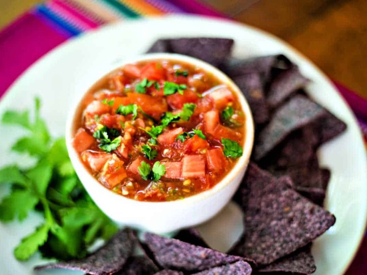 fresh tomato salsa on a white platter with cilantro and blue corn tortilla chips
