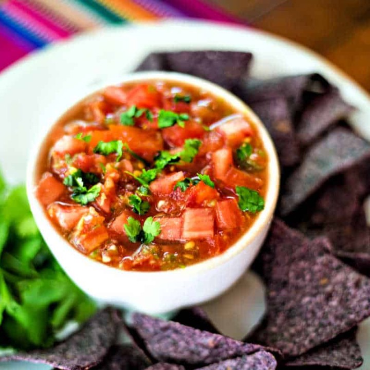 fresh tomato salsa on a white platter with cilantro and blue corn tortilla chips