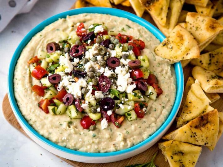 Mediterranean Layered Dip with pita triangles on a wooden board