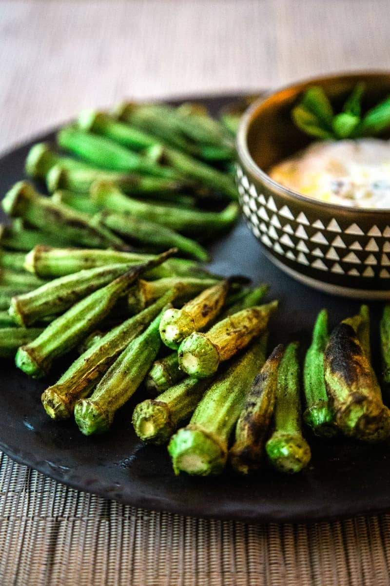 grilled whole okra pods on a black platter with dipping sauce