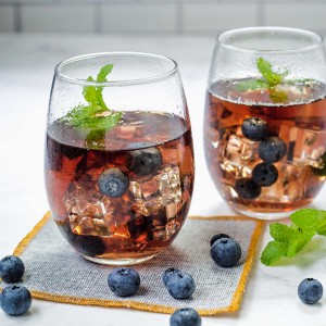 two glasses of blueberry tea with blueberries and mint springs on a counter.