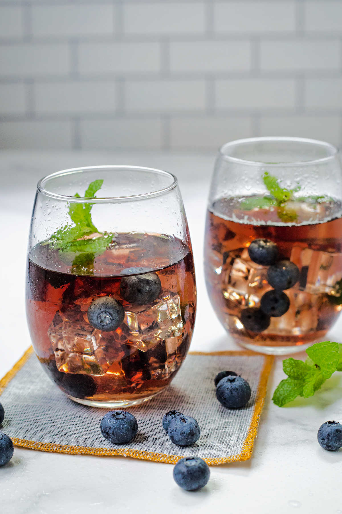 two glasses of blueberry tea with blueberries and mint springs on a counter.