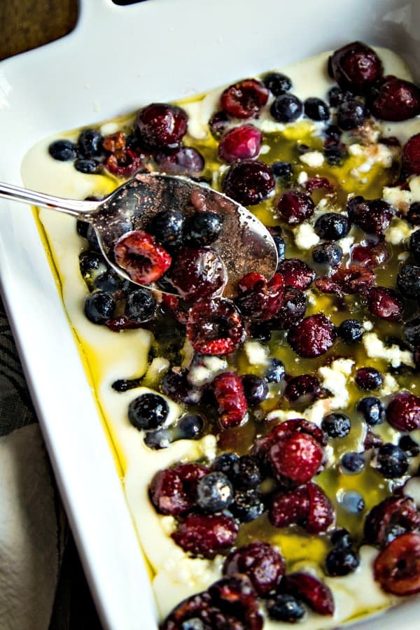 spooning fresh fruit over cobbler batter in a white baking dish