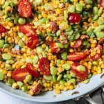 a skillet of corn succotash with a wooden spoon.