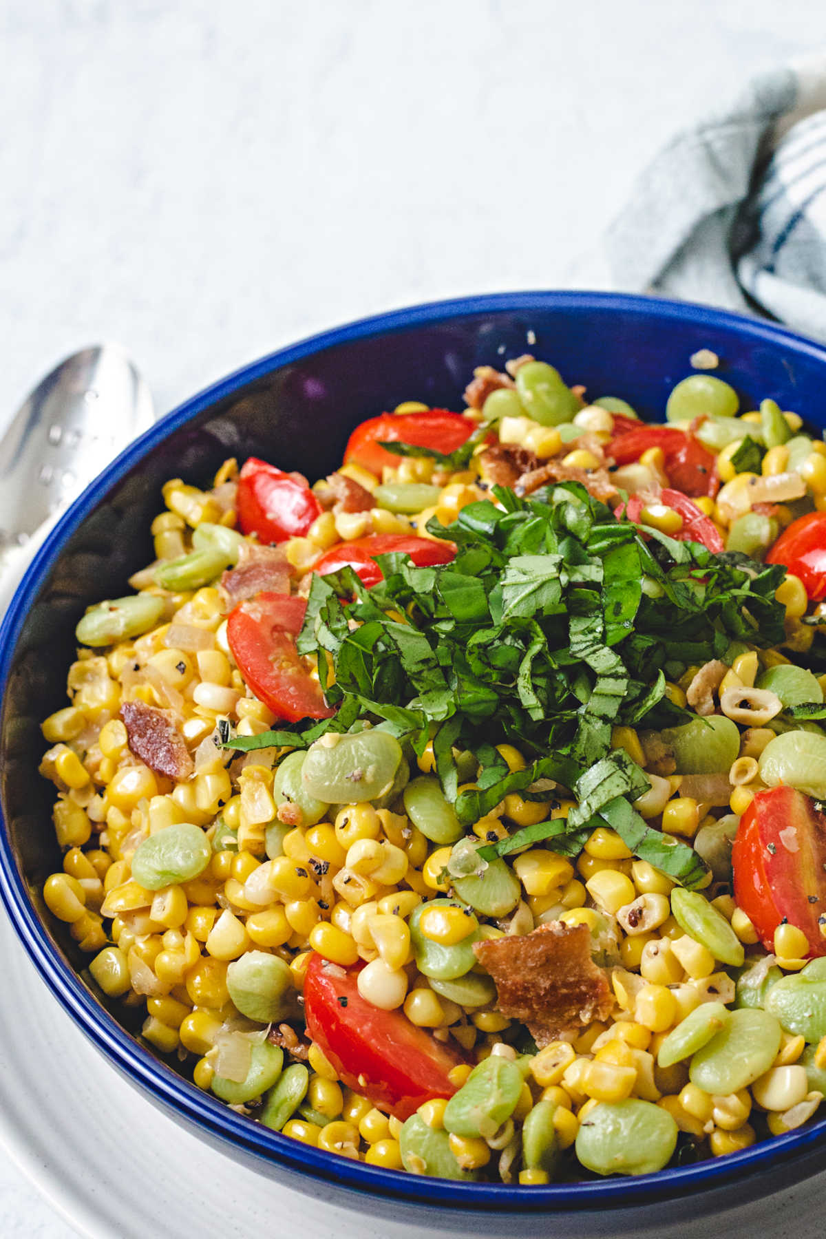 corn succotash garnished with a mound of basil chiffonade in a blue bowl on top of a white plate.