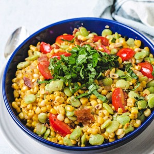 corn succotash garnished with a mound of basil chiffonade in a blue bowl on top of a white plate.