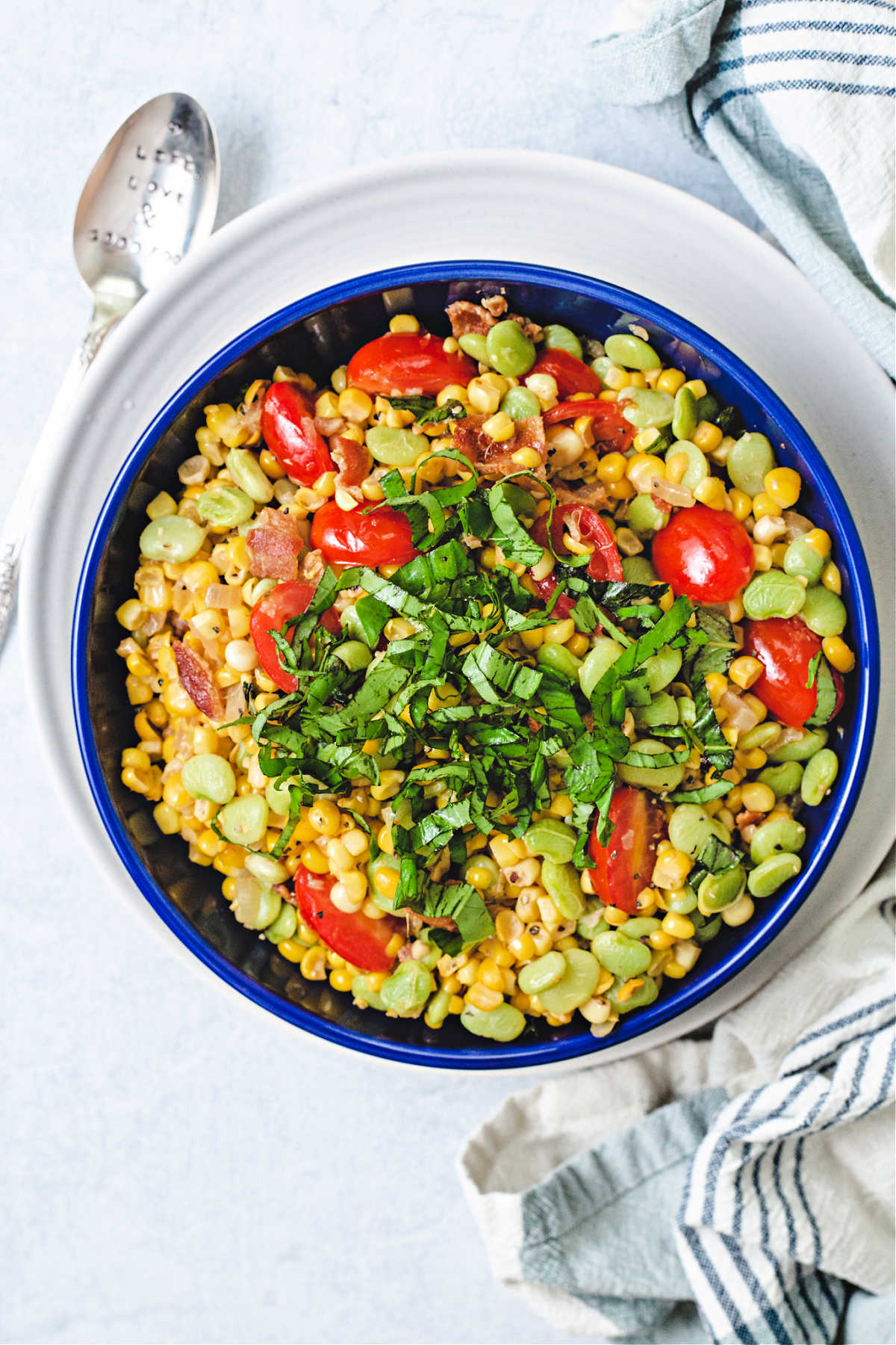 corn succotash garnished with a mound of basil chiffonade in a blue bowl on top of a white plate.