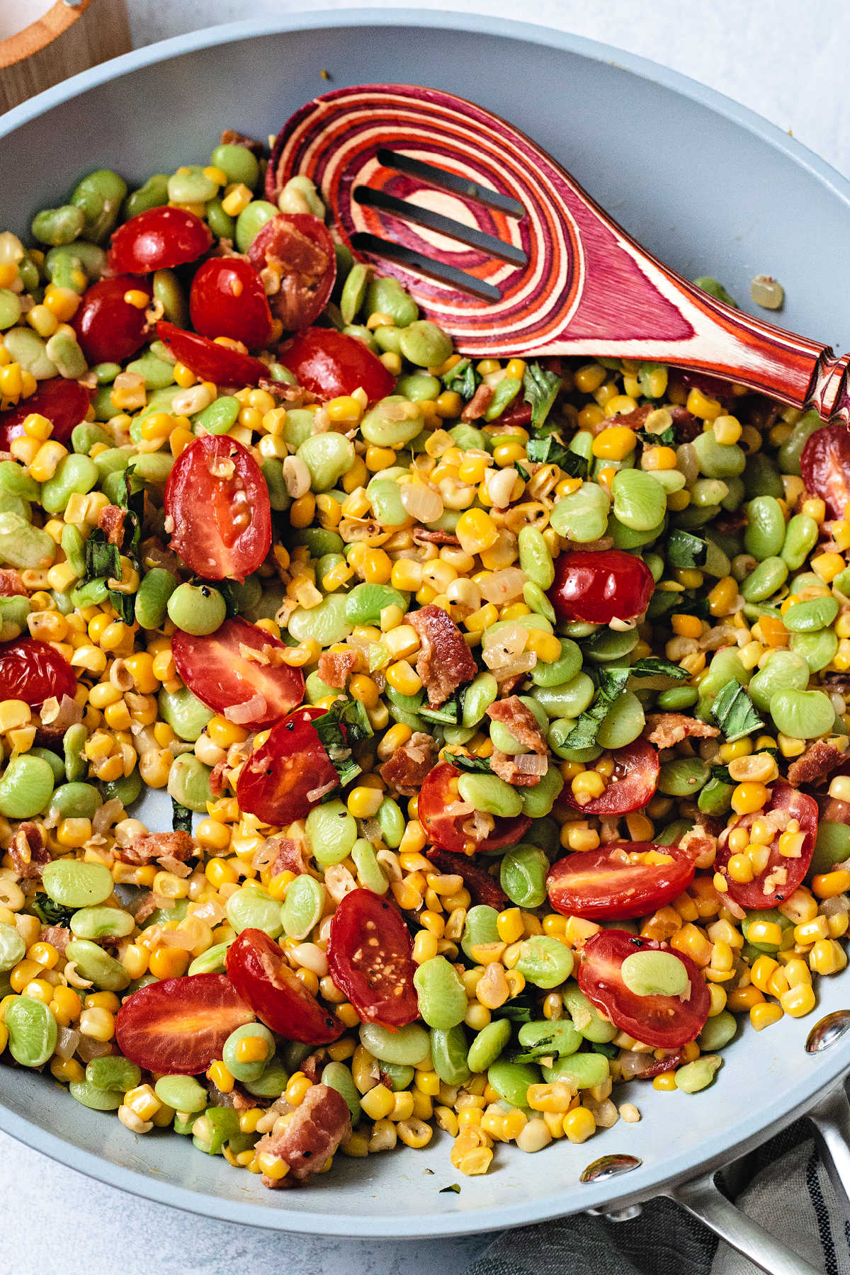 corn succotash with tomatoes and basil in a frying pan with a spoon.