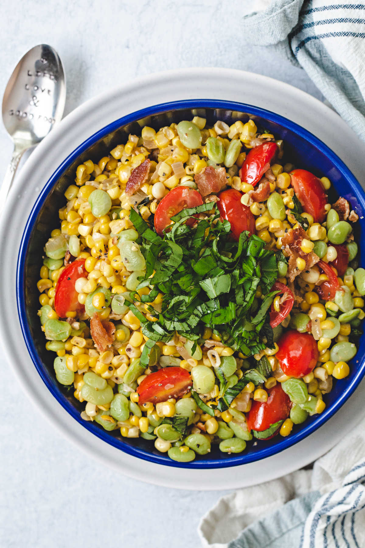 corn succotash garnished with a mound of basil chiffonade in a blue bowl on top of a white plate.
