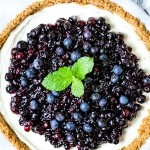 a no bake blueberry cheesecake in a white pie plate with a mint sprig garnish.