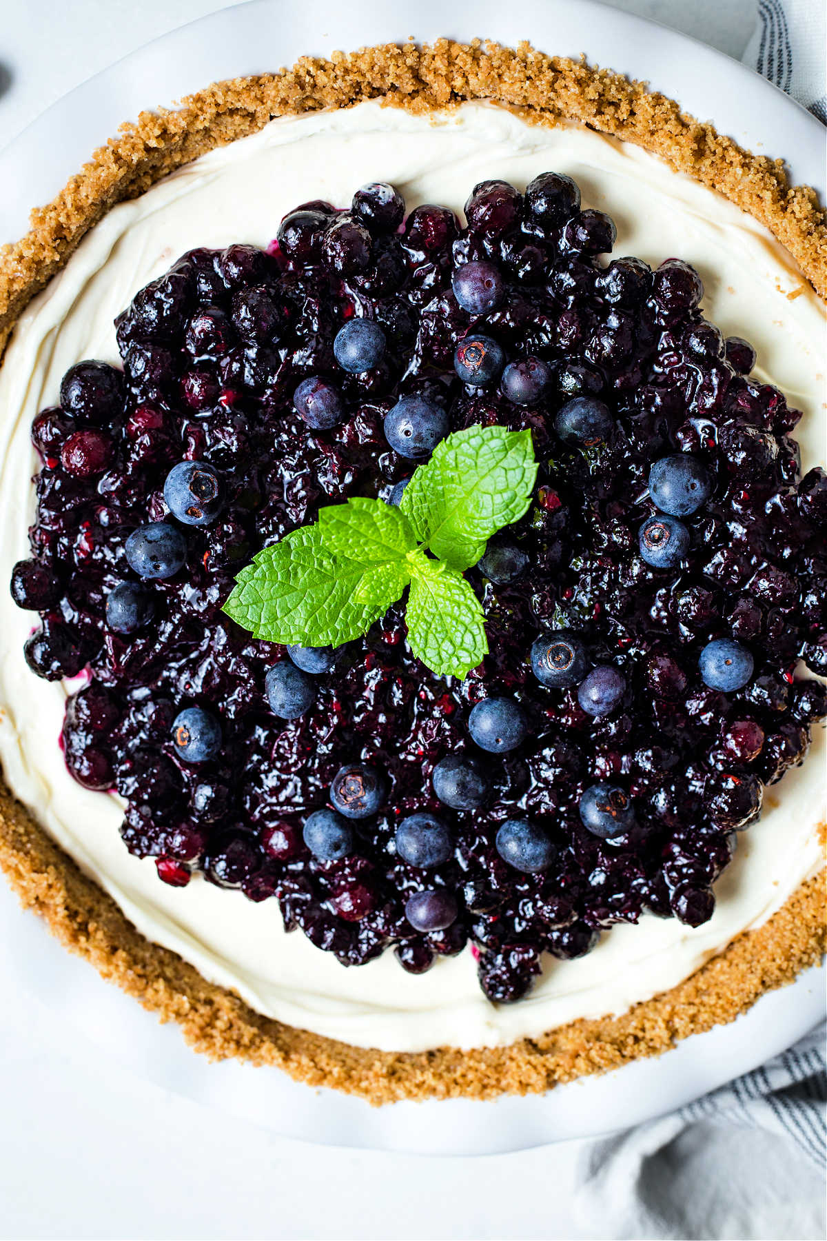top down view of a no bake blueberry cheesecake in a white pie plate with a mint sprig garnish.