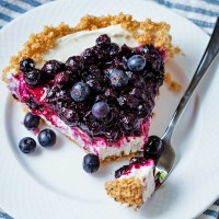a bite of no bake blueberry cheesecake on a fork alongside a slice on a white plate.