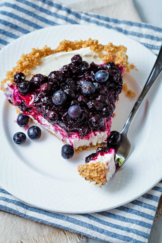 a bite of no bake blueberry cheesecake on a fork alongside a slice on a white plate.
