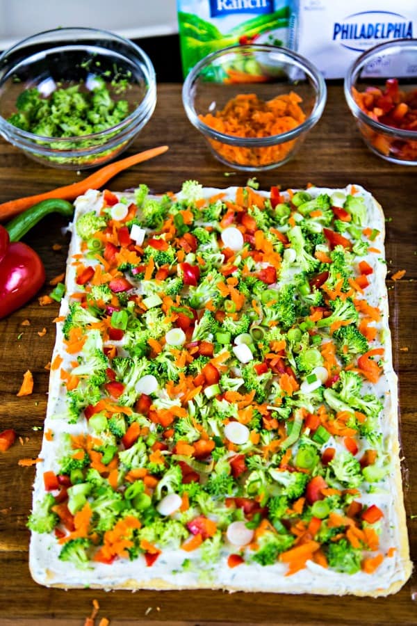 baked crescent dough with ranch cream cheese and chopped veggies on a wooden board