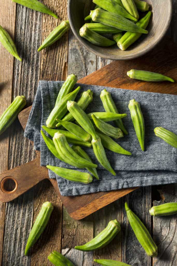 whole pods of fresh okra on a wooden cutting board