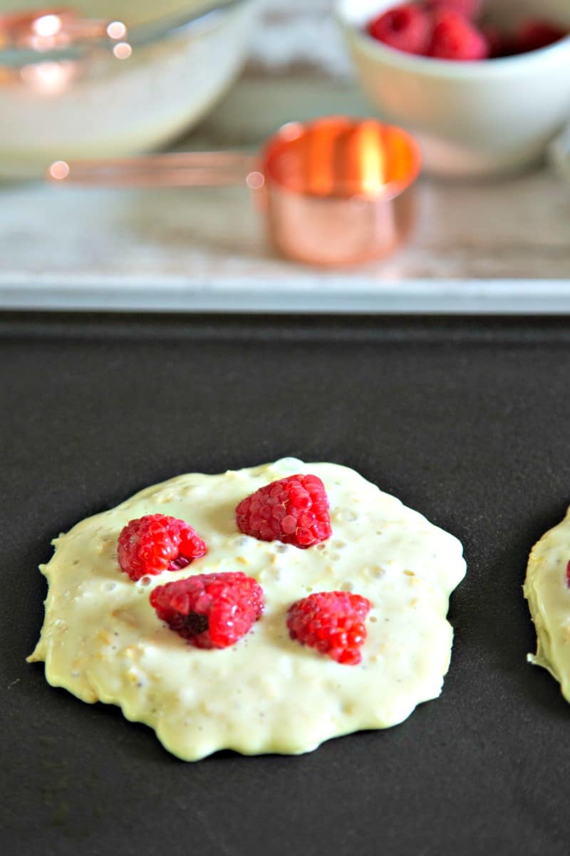 pancakes cooking on an electric griddle with raspberries on top