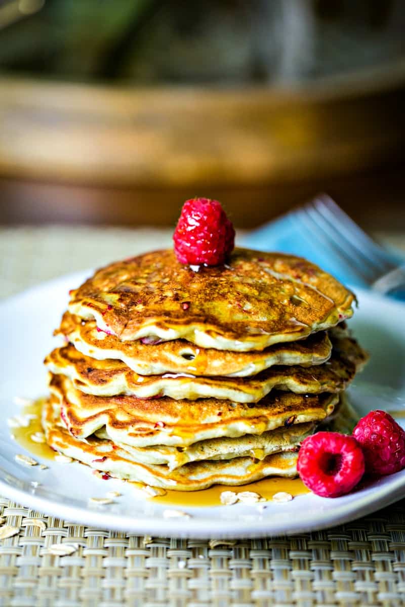 stack of pancakes on white plate with raspberries