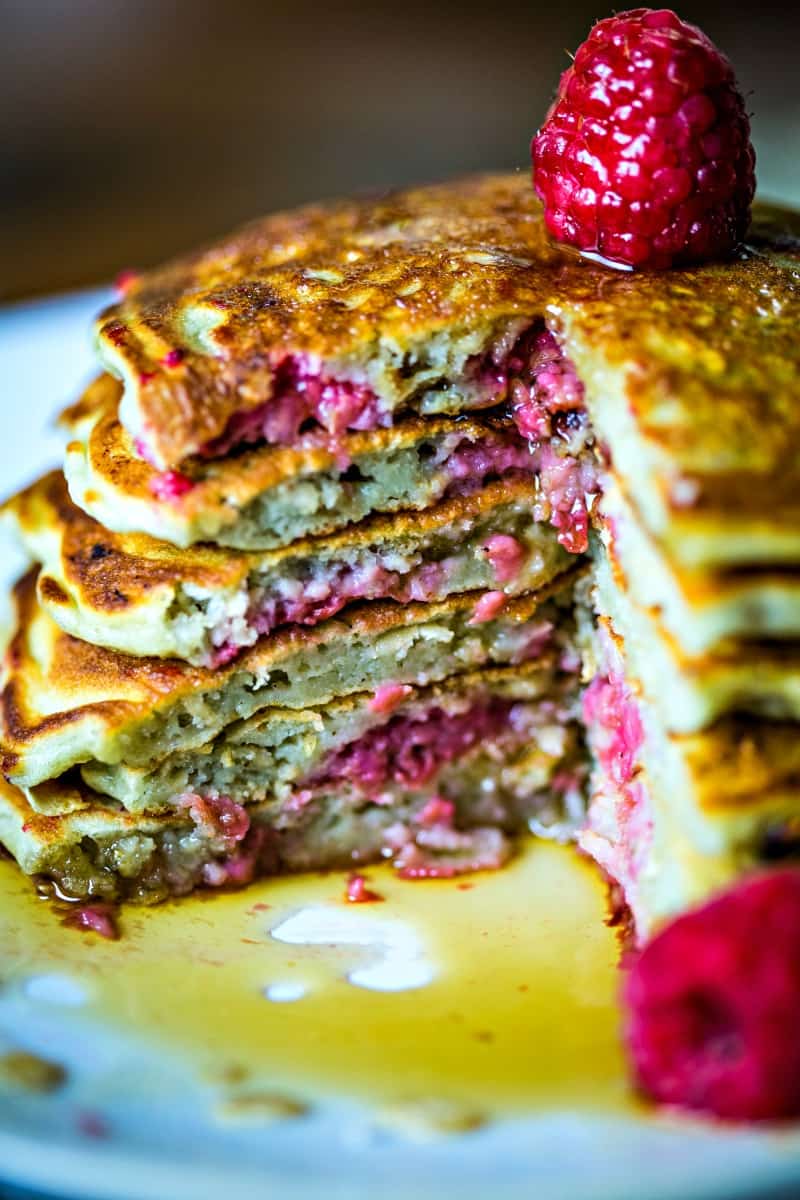 a stack of pancakes with a pie shape cut out with maple syrup dripping onto the white plate