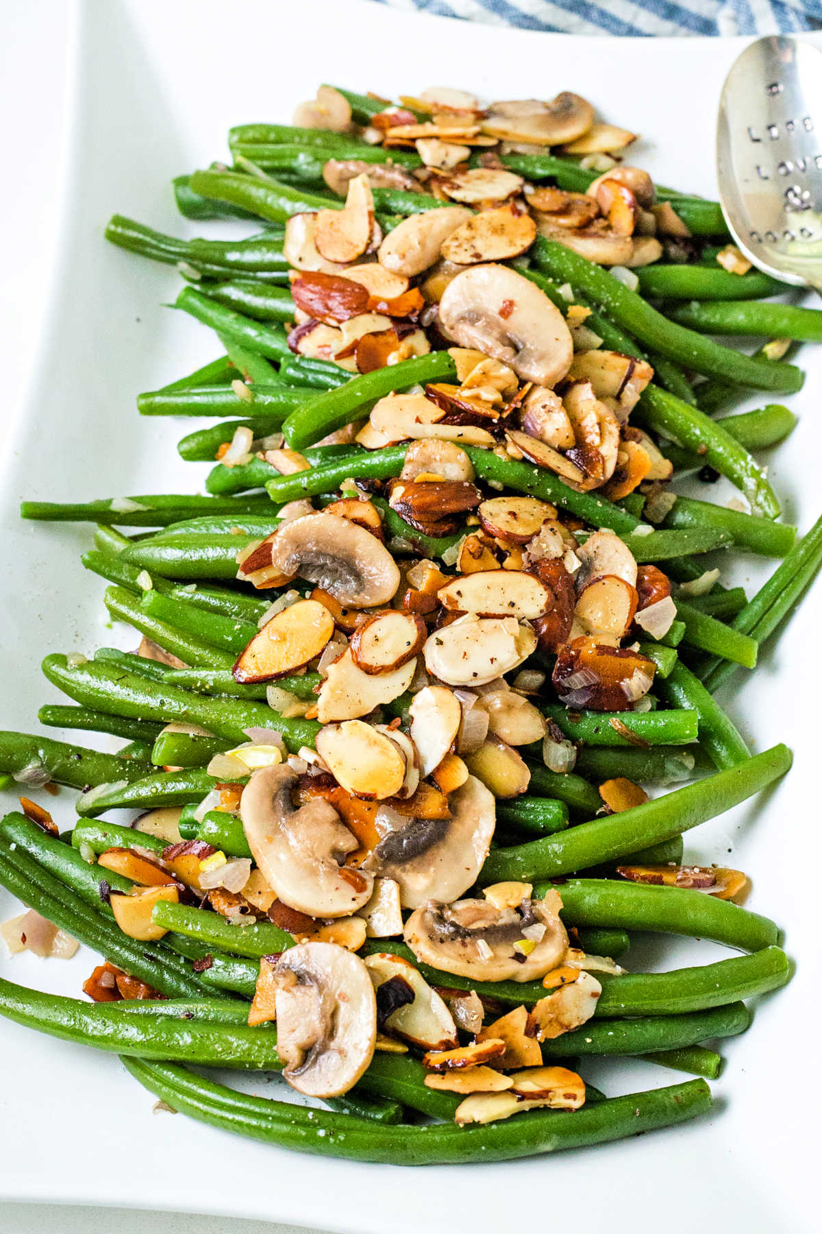 green bean almondine on a white serving platter with almonds and mushrooms scattered on top.