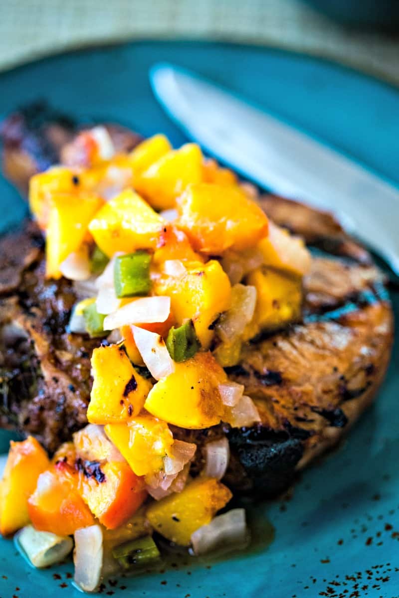 grilled pork chop on a blue plate with peach salsa on top