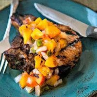 grilled pork chop with peaches on a blue plate with knife and fork