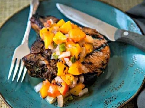 grilled pork chop with peaches on a blue plate with knife and fork