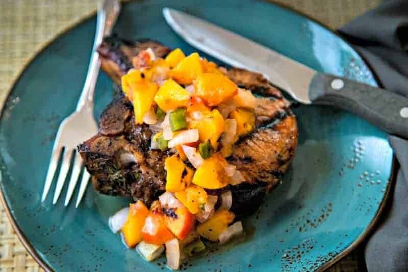 grilled pork chop with peaches on a blue plate with knife and fork