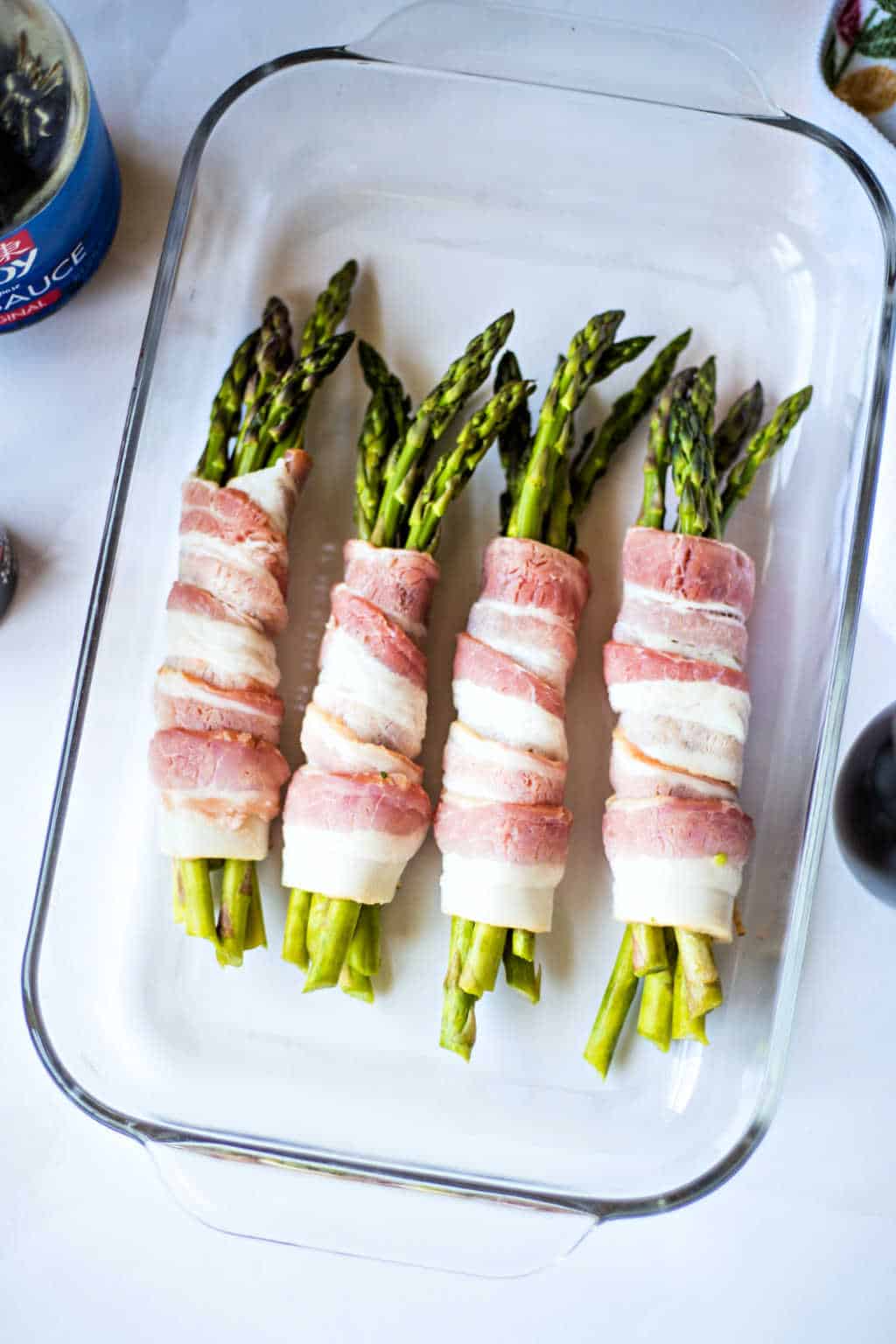 asparagus wrapped in raw bacon in a baking dish