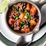 a soup mug filled with black bean and sweet potato chili sitting on a white plate.