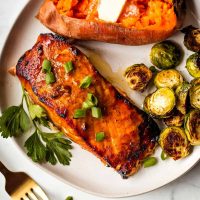 grilled salmon with brussel sprouts and a baked sweet potato on a white plate