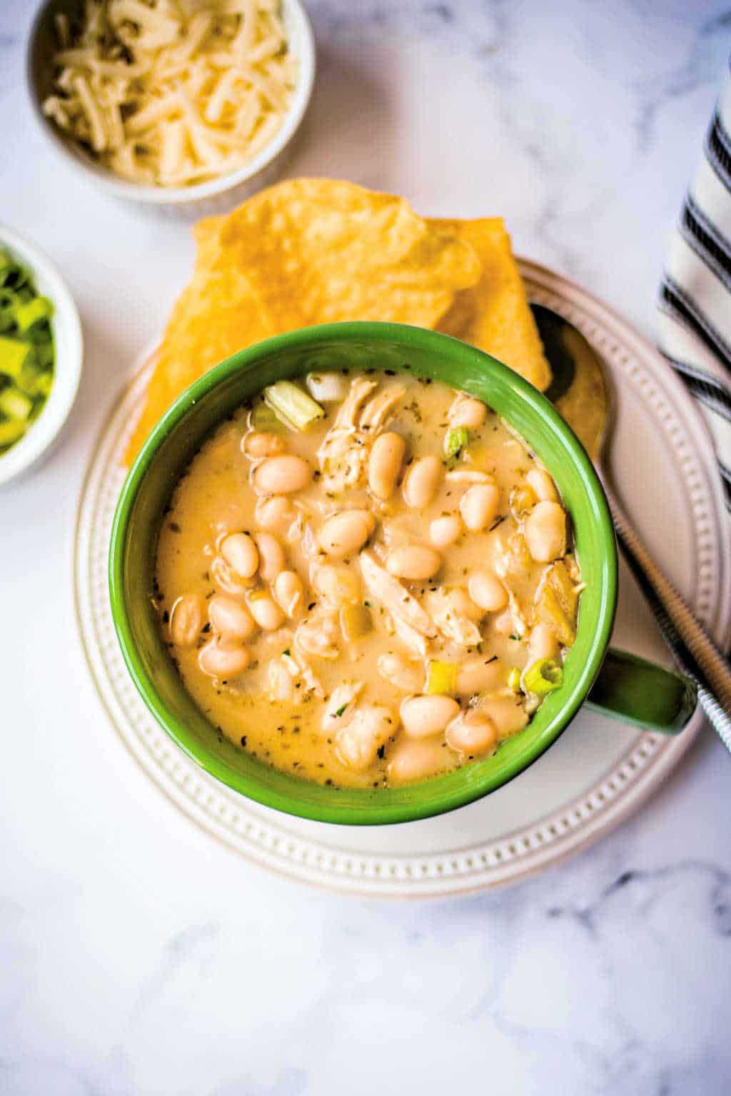 white chicken chili in a green soup bowl with condiments