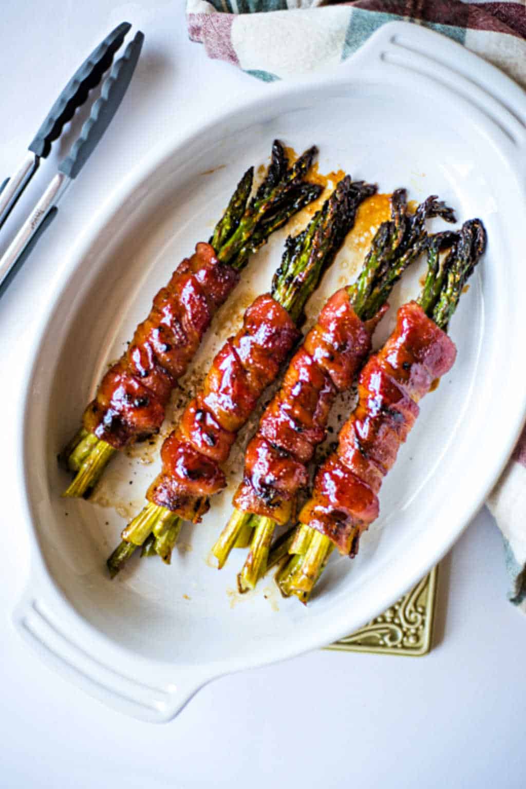 bacon wrapped asparagus bundles in a white baking dish