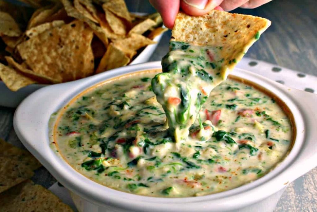 A person dipping a tortilla chip into Spinach Artichoke Dip