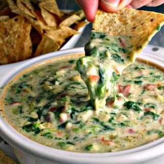 A person dipping a tortilla chip into Spinach Artichoke Dip