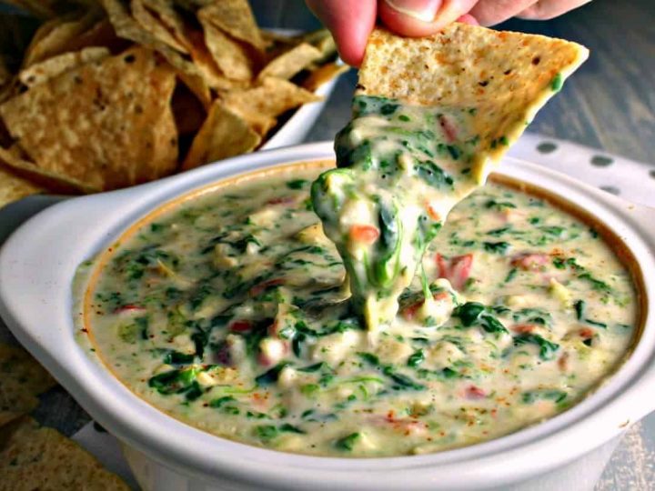 A person dipping a tortilla chip into Spinach Artichoke Dip