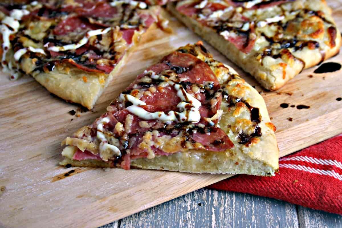 A slice of pizza sitting on top of a wooden cutting board, with Salami Pizza with Garlic Dijon Aioli