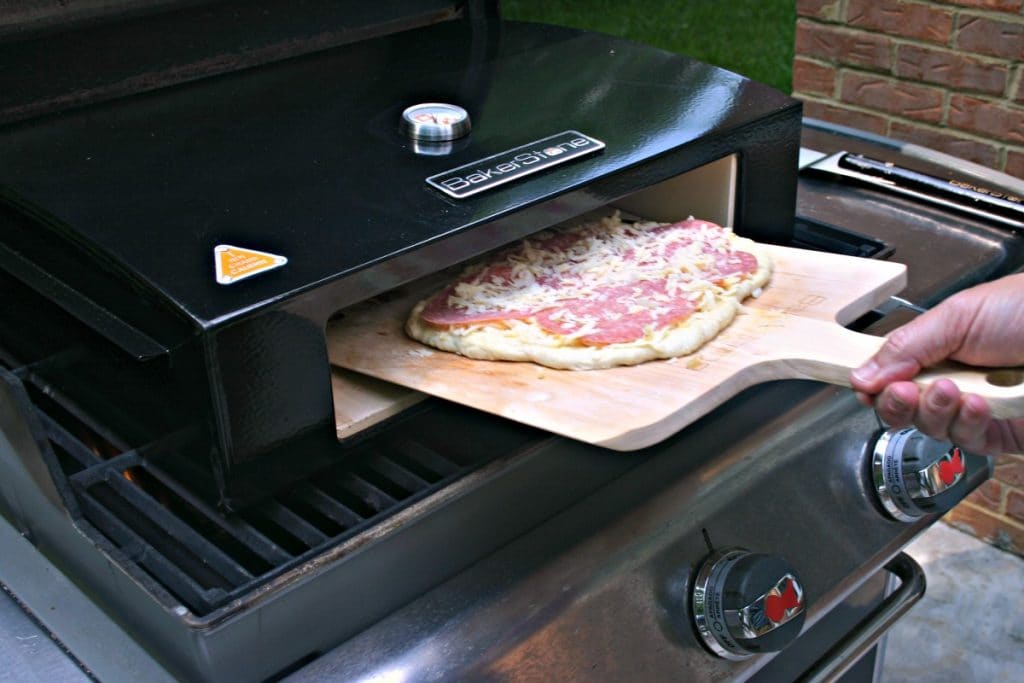 Sliding a pizza into a grill-top pizza oven