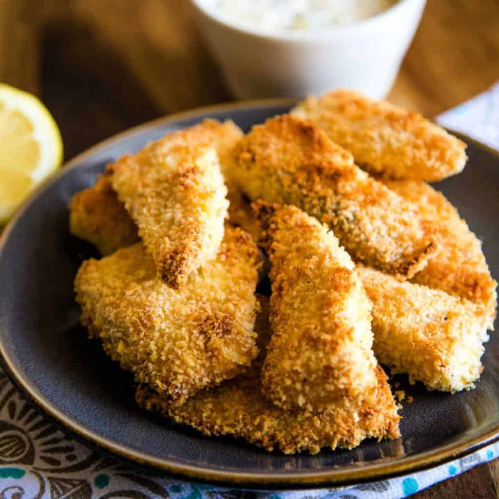 breaded oven fried fish on a gray plate with lemon garnish